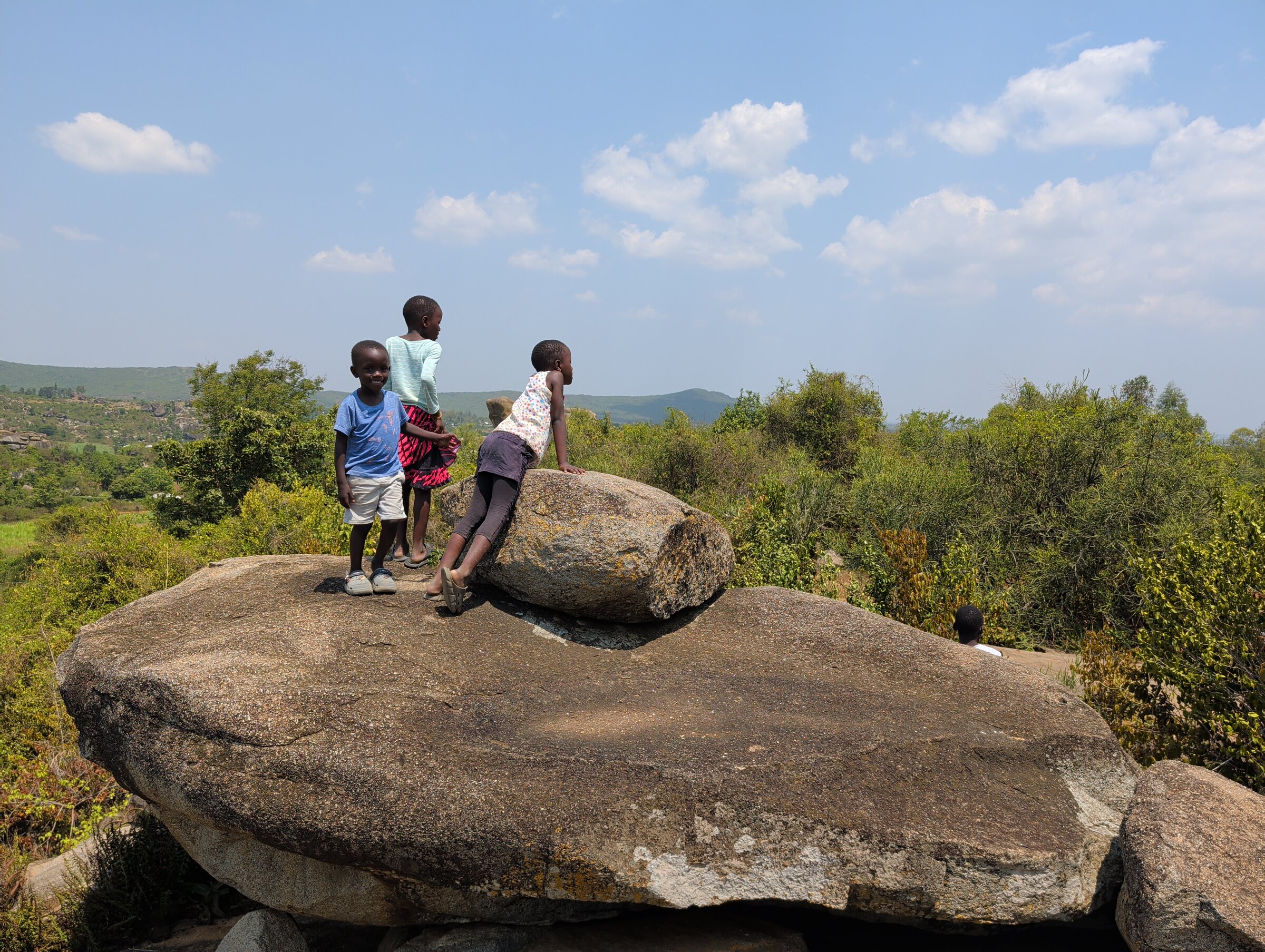 Drei Kids auf einer Felsformation vor einer schönen, weitläufigen Landschaft